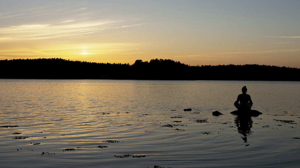 Person sitzt still im See bei Sonnenuntergang, ganz bei sich